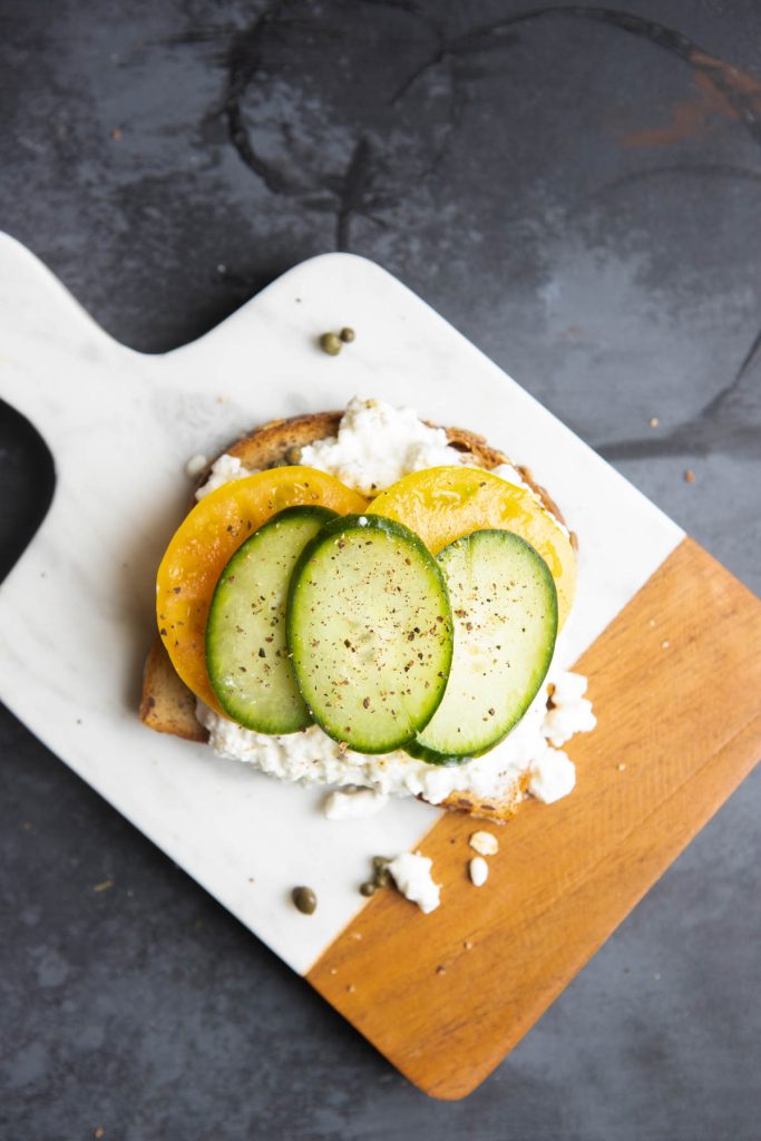 sliced heirloom tomatoes and cucumber and capers topped on cottage cheese spread on toasted bread