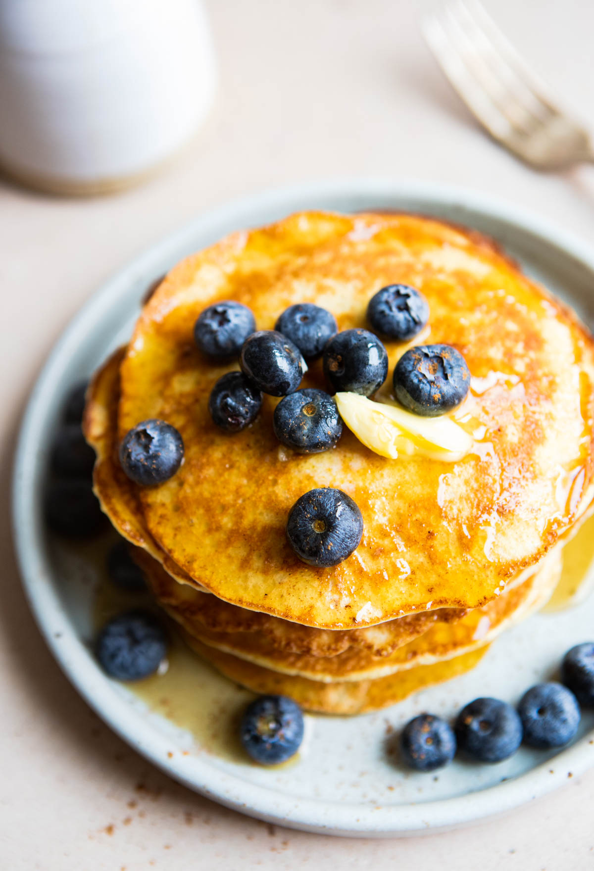 stack of golden brown protein pancakes on a plate topped with blueberries and maple syrup 