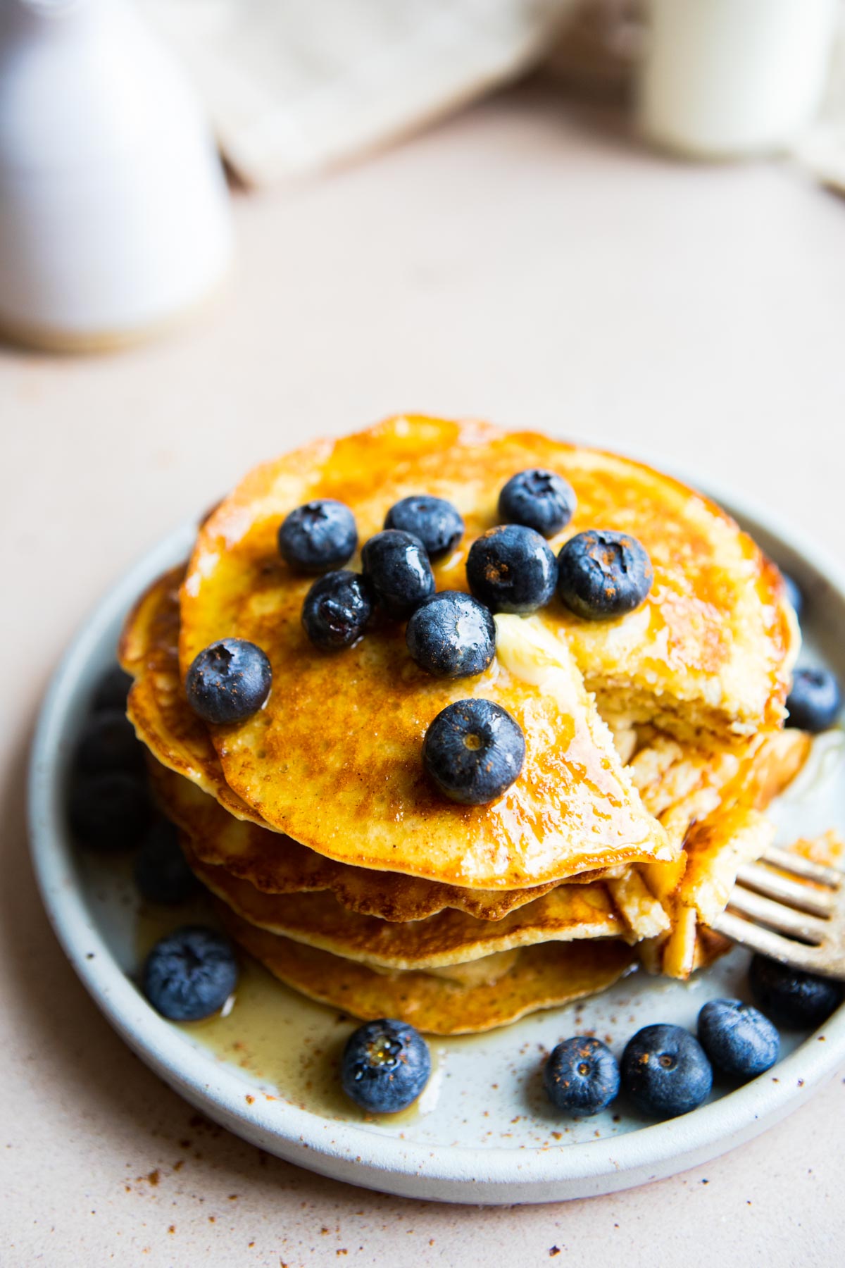 fork next to a stack of pancakes topped with blueberries 