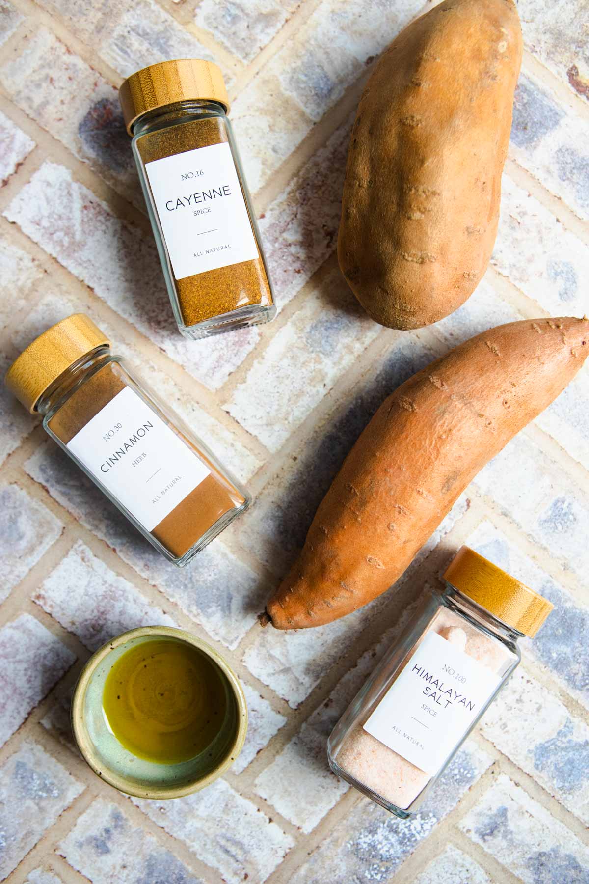 ingredients to make roasted spicy sweet potatoes on a brick background