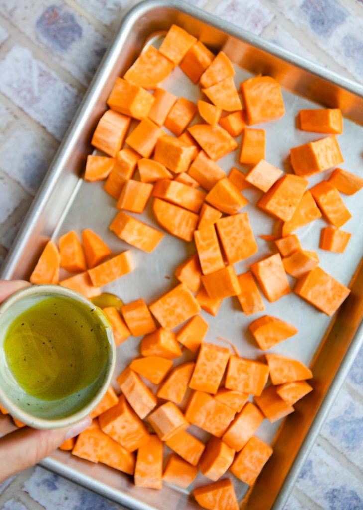 peeled and cubed sweet potatoes on a sheet pan with olive oil drizzled on top