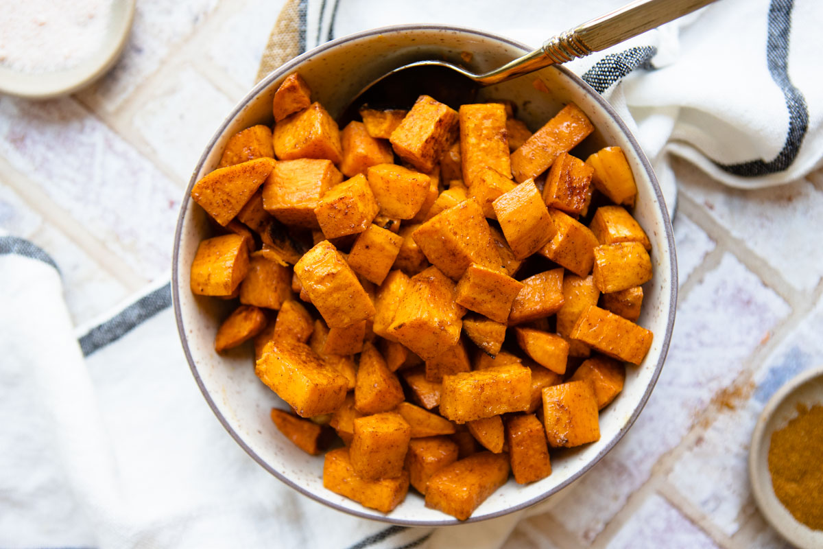 roasted sweet potatoes served in a beige bowl with a antique serving spoon