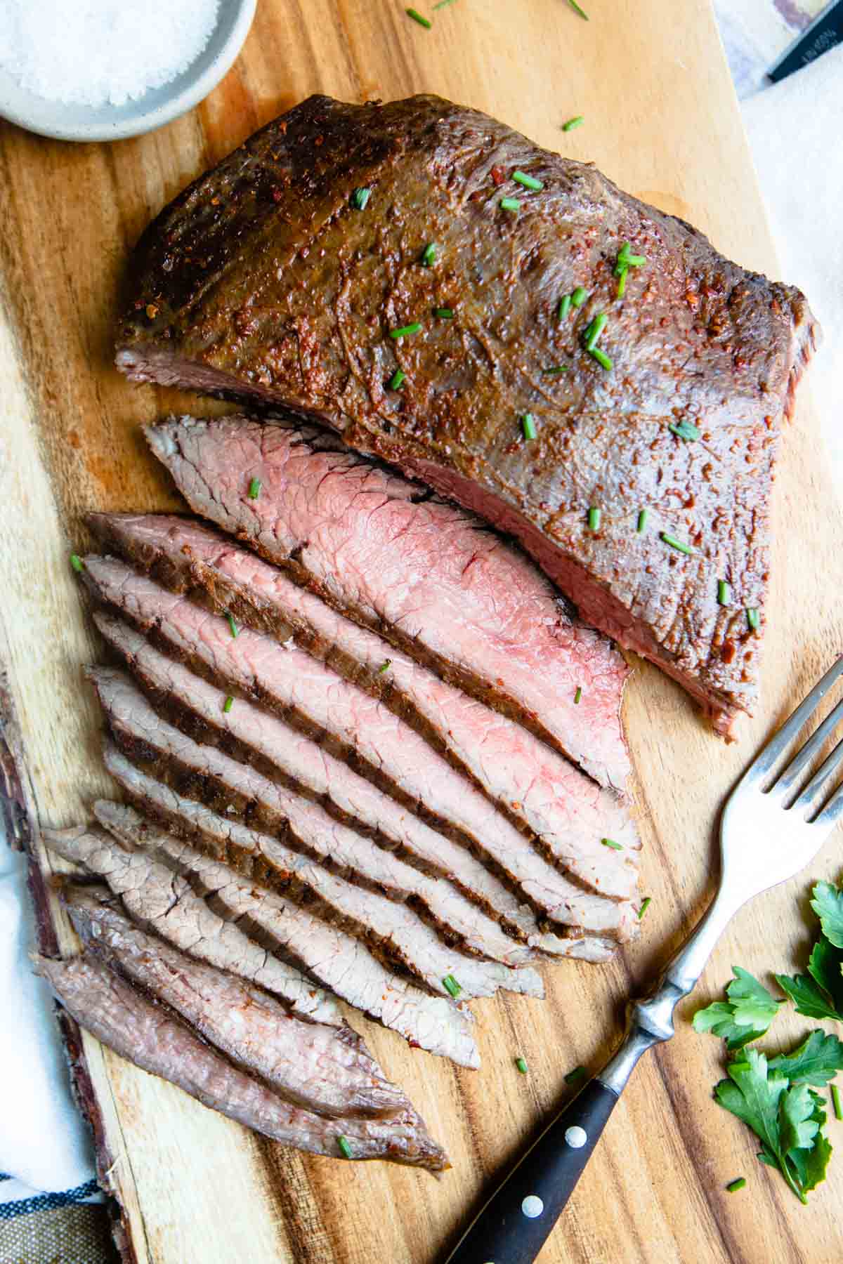 Seasoned flank steak cooked in the air fryer resting on a cutting board with thin slices cut away. 