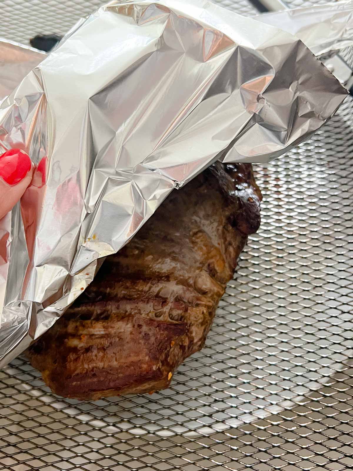 Aluminum foil covering a piece of steak prepared in the air fryer.