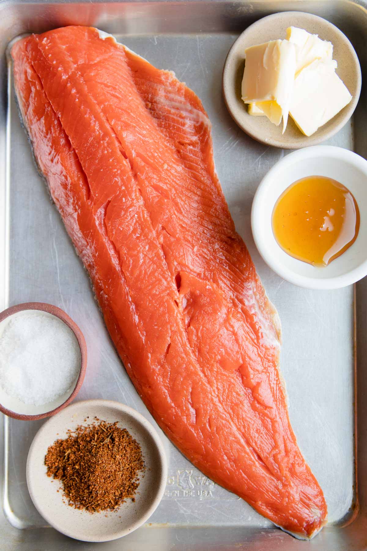 raw salmon filet, cajun spices, honey and butter on a baking sheet