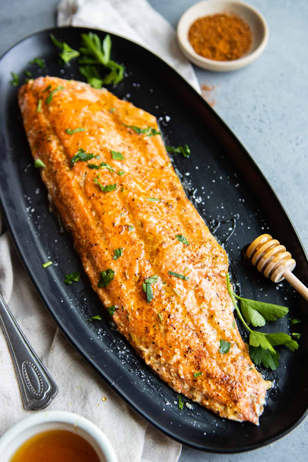 salmon filet cooked with cajun joney butter set on a black platter garnished with parsley 