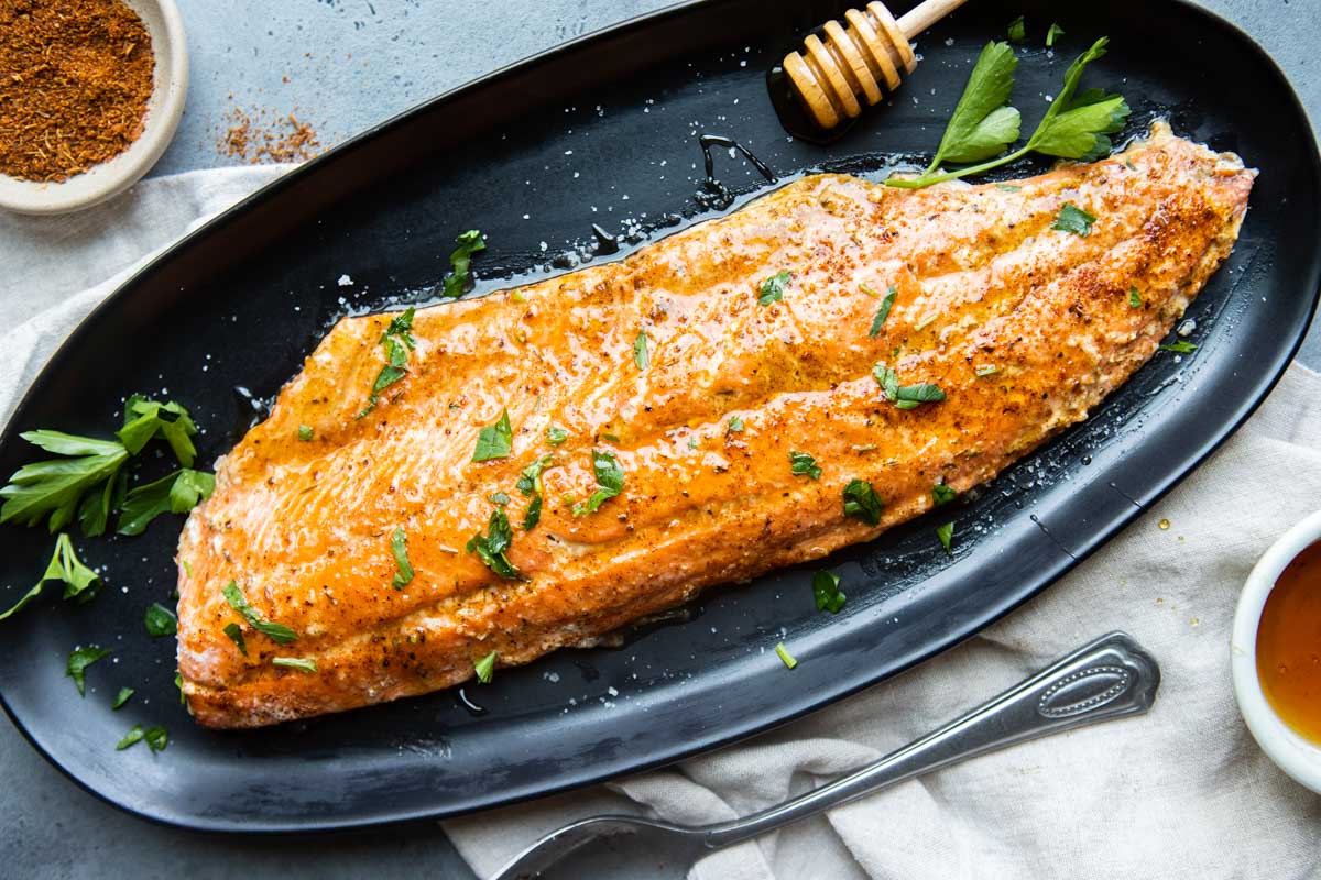 cajun honey butter salmon on a black dish next to a small bowl of dry cajun spices