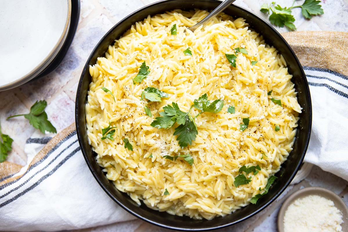 Tasty orzo pasta ready to serve from a large serving bowl with a spoon resting in it.