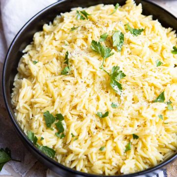 Large bowl of fluffy orzo pasta with garnish of parsley pieces on top.