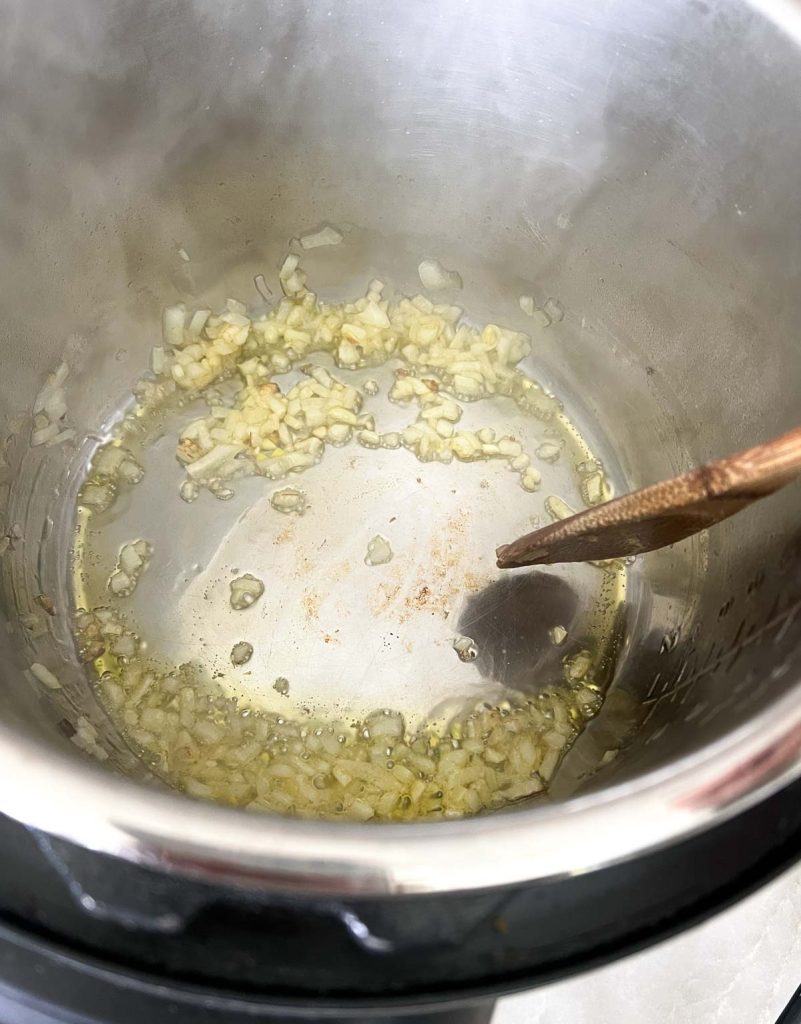 Wooden spoon stirring diced onion in the instant pot.