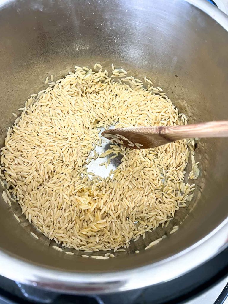 Wooden spoon stirring orzo pasta in an instant pot.