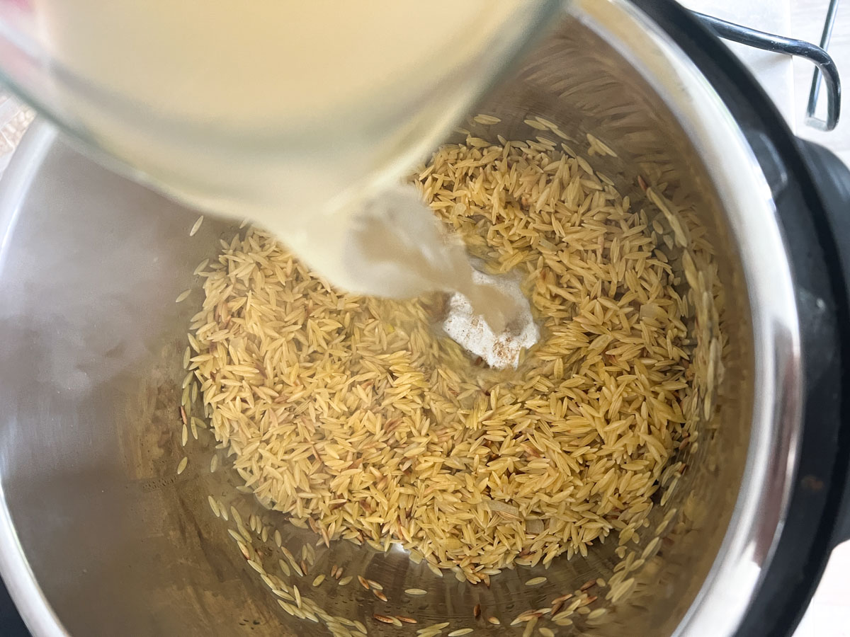 Broth being added to an instant pot with orzo pasta inside.