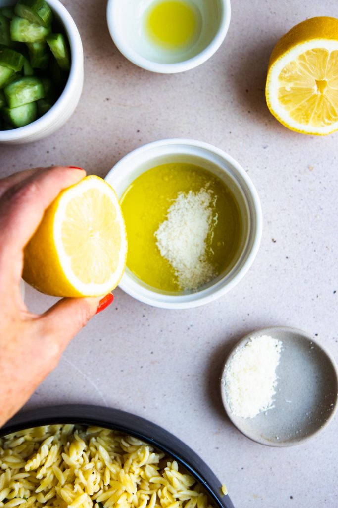 Hand squeezing a lemon over oil and parmesan to make a homemade dressing.