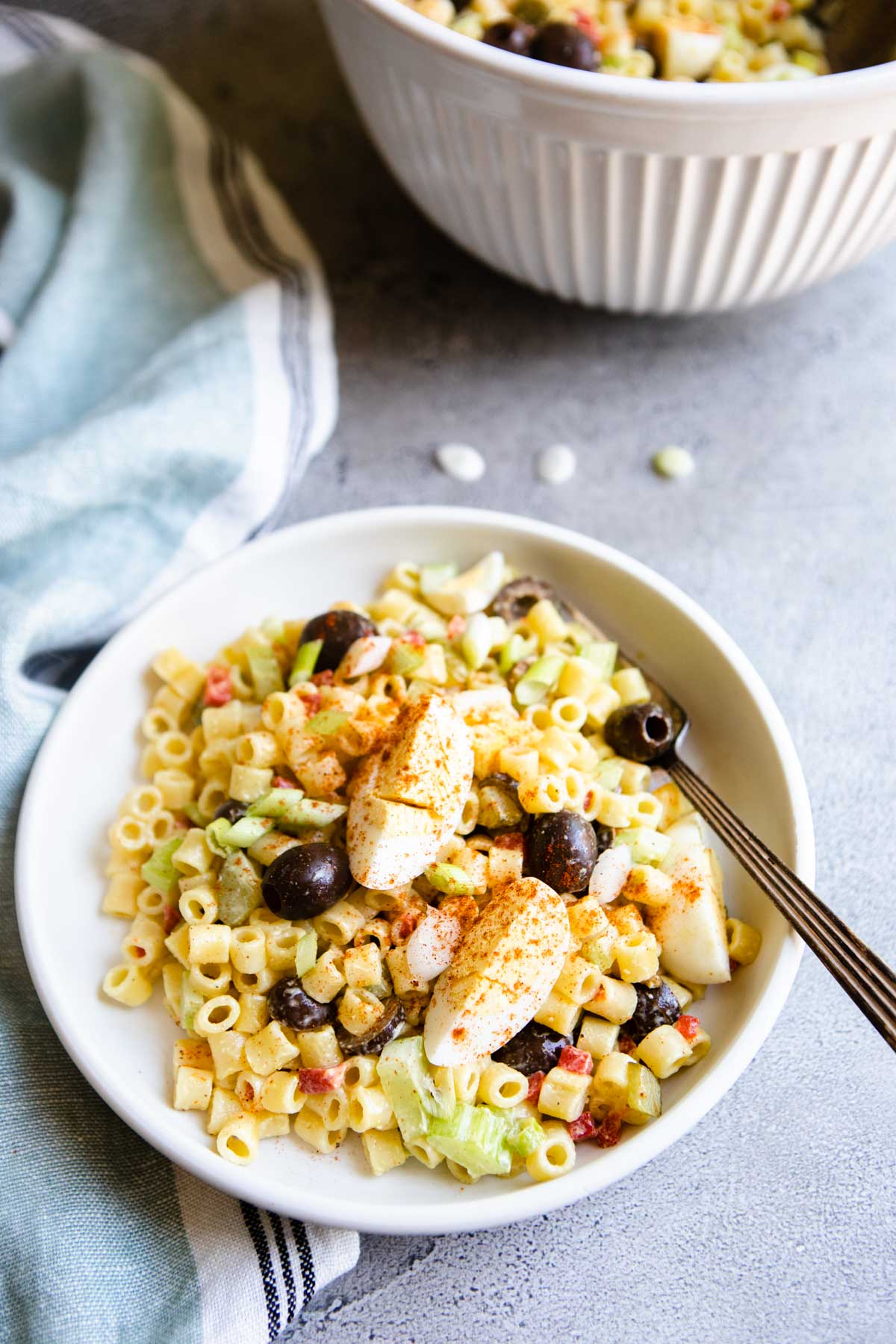 Southern Macaroni Salad with a fork resting in it filled with hardboiled eggs, olives and green onions.