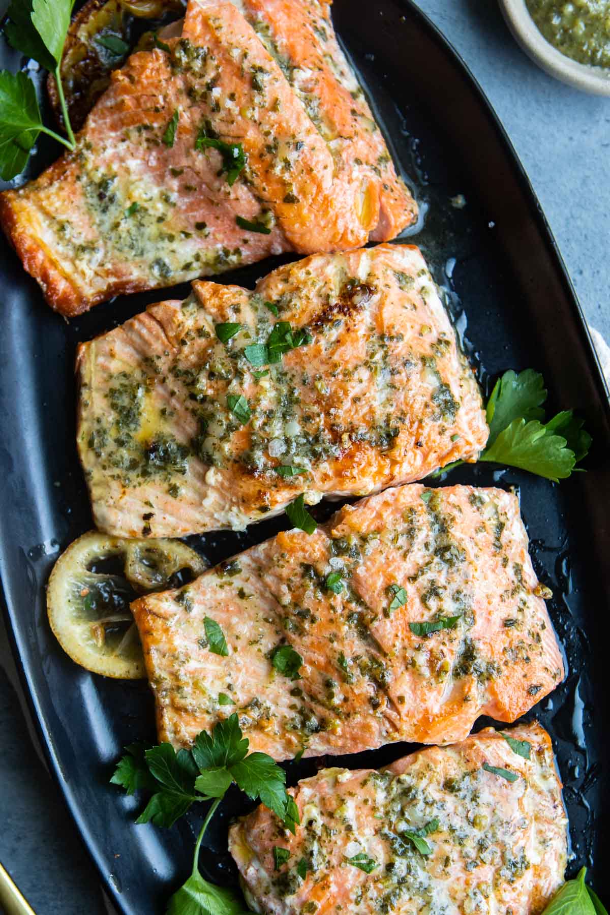 Pesto butter salmon served on an oval serving platter with lemon slices and parsley garnishes.