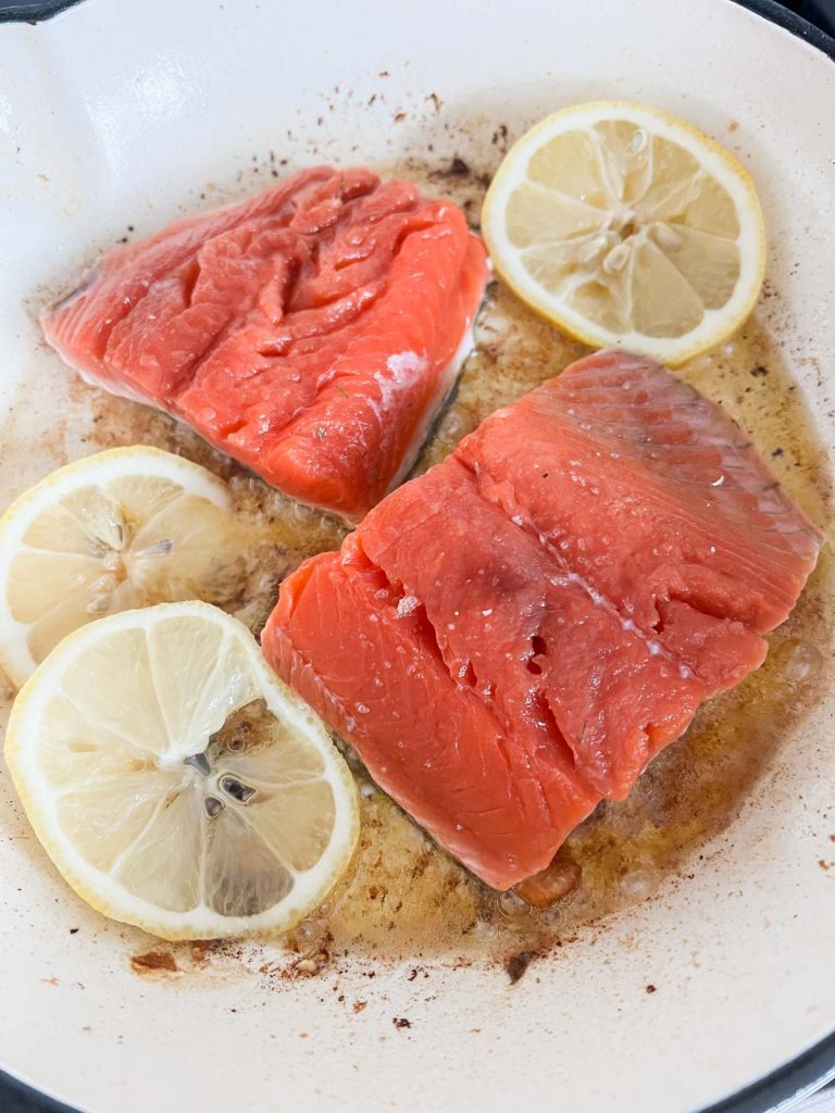 Fresh lemon slices added to a pan with salmon filets, skin side down.