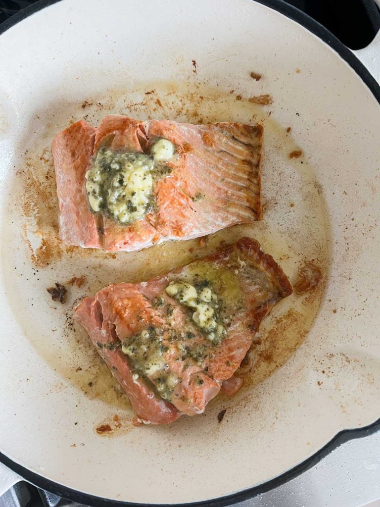 Pesto butter topping salmon filets in a pan.