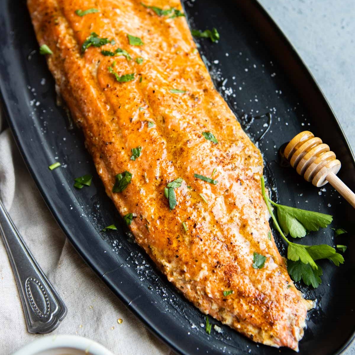 Cajun honey butter salmon on a black serving platter garnished with parsley and honey.