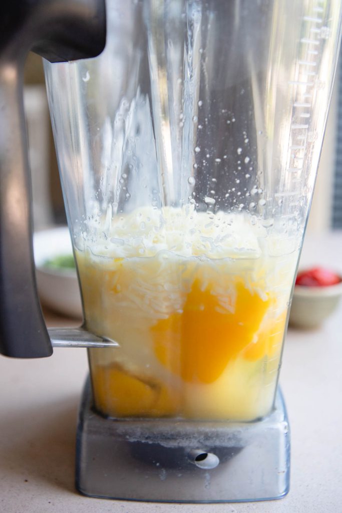Side view of a blender filled with eggs and shredded cheese.