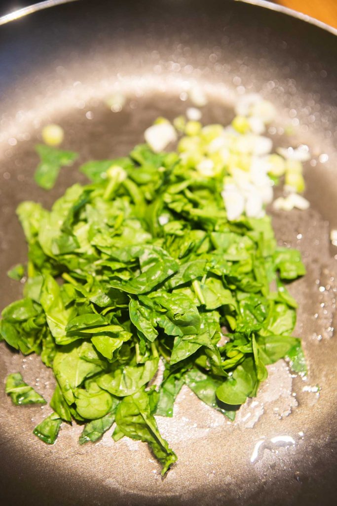 Onions and spinach sauteing in a skillet.