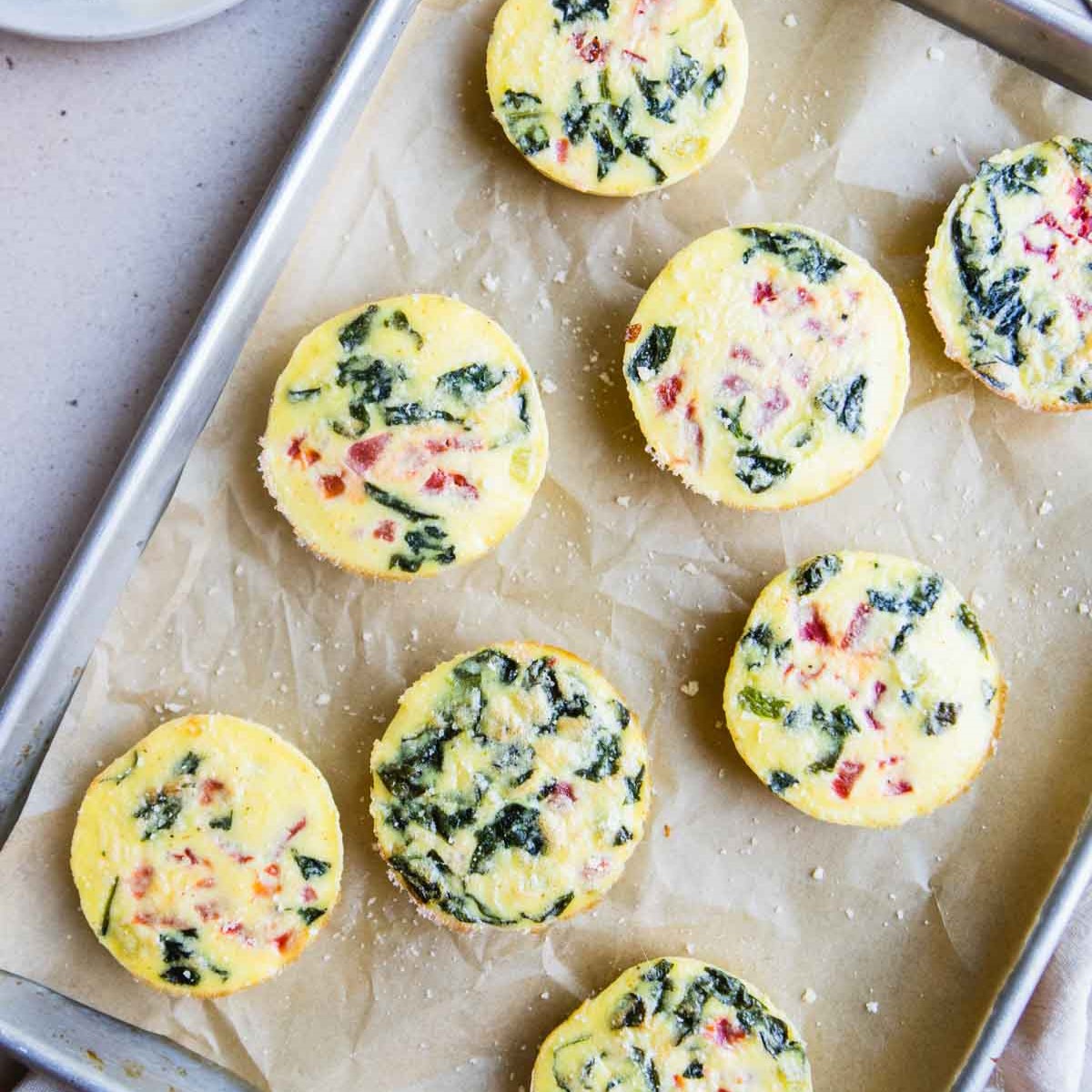 Baking dish with colorful, veggie filled egg bites laying on parchment paper.