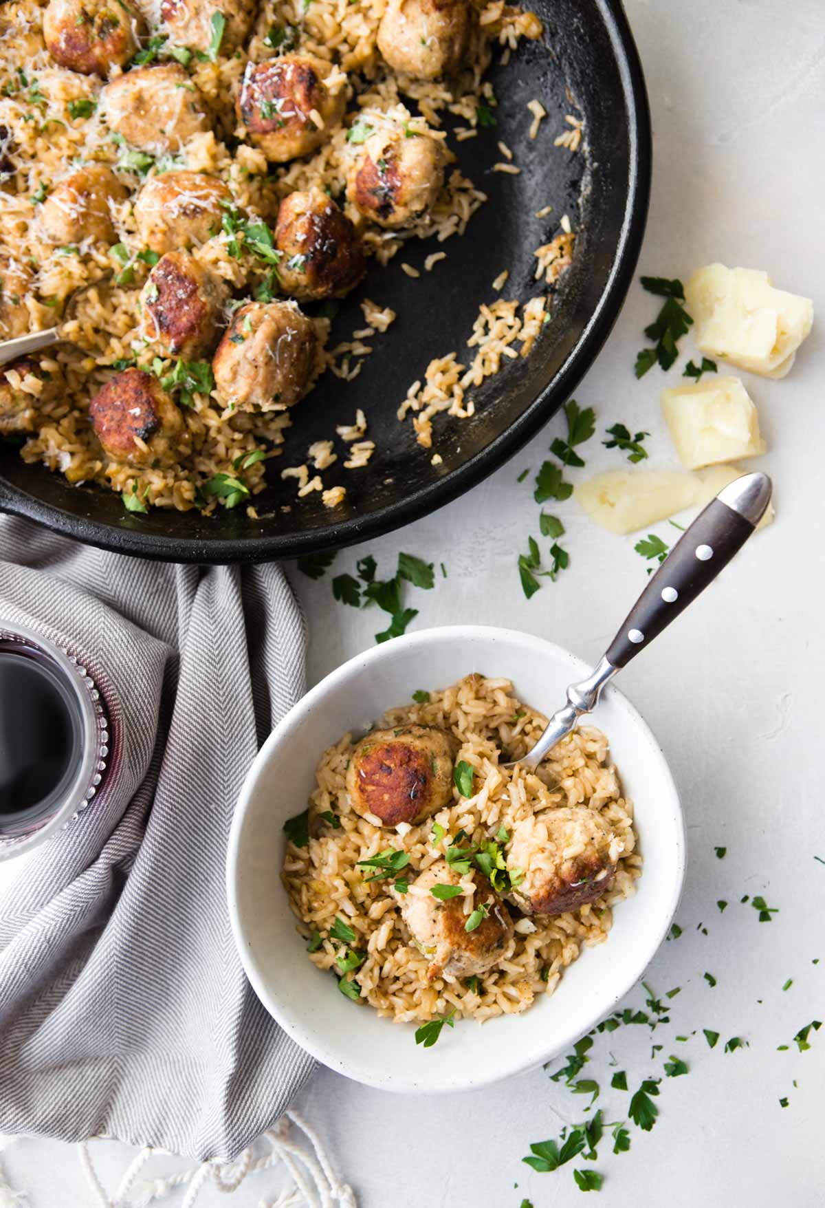 a small bowl filled with brown rice and cooked turkey meatballs, next to a cast iron skillet 