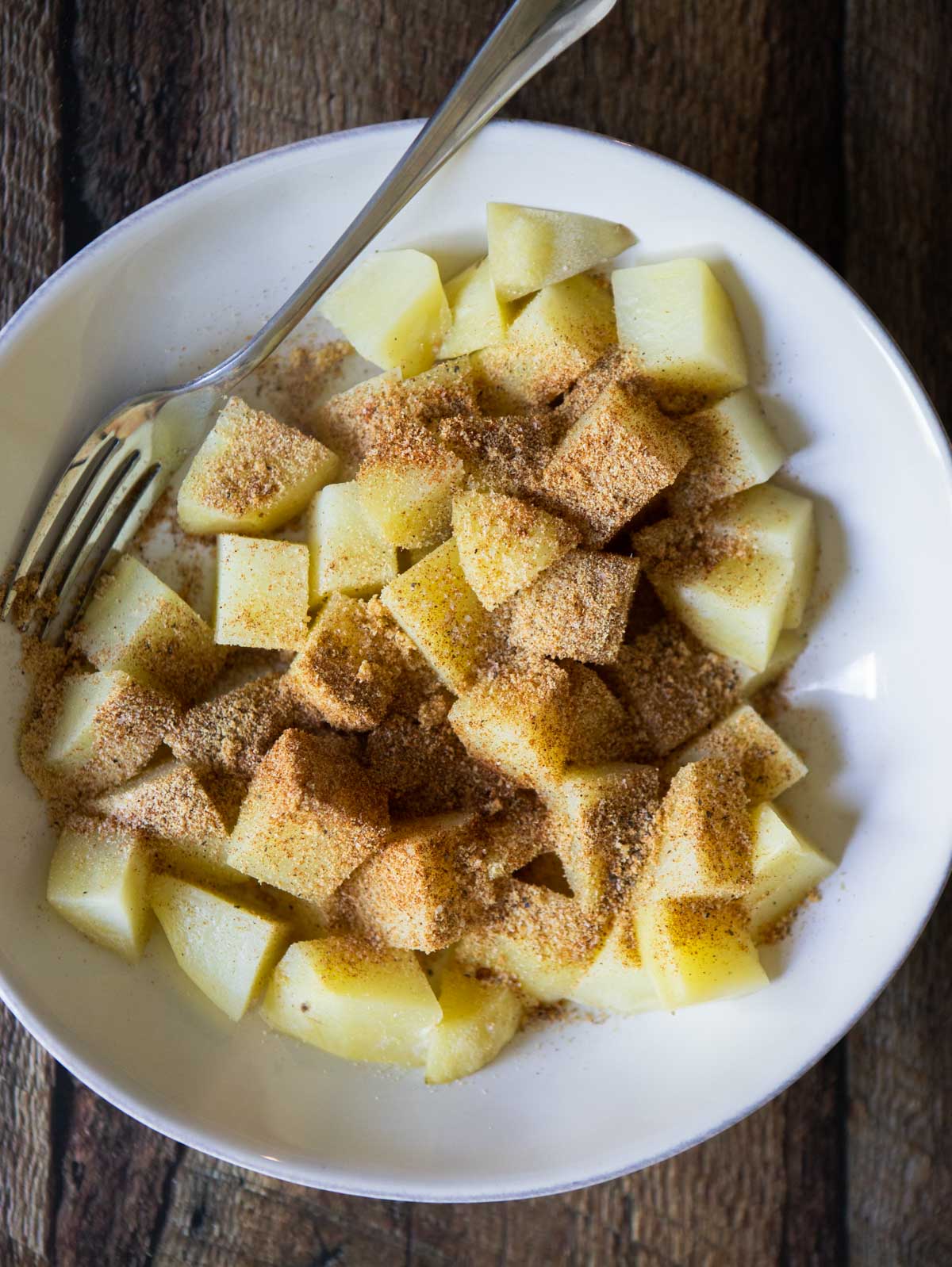 parcooked potatoes in a white bowl sprinkled with herb and spice blend 