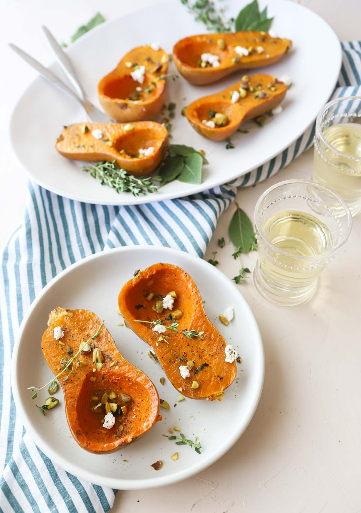 a white platter filled with roasted honeynut squash, garnished with goat cheese and pistachios 