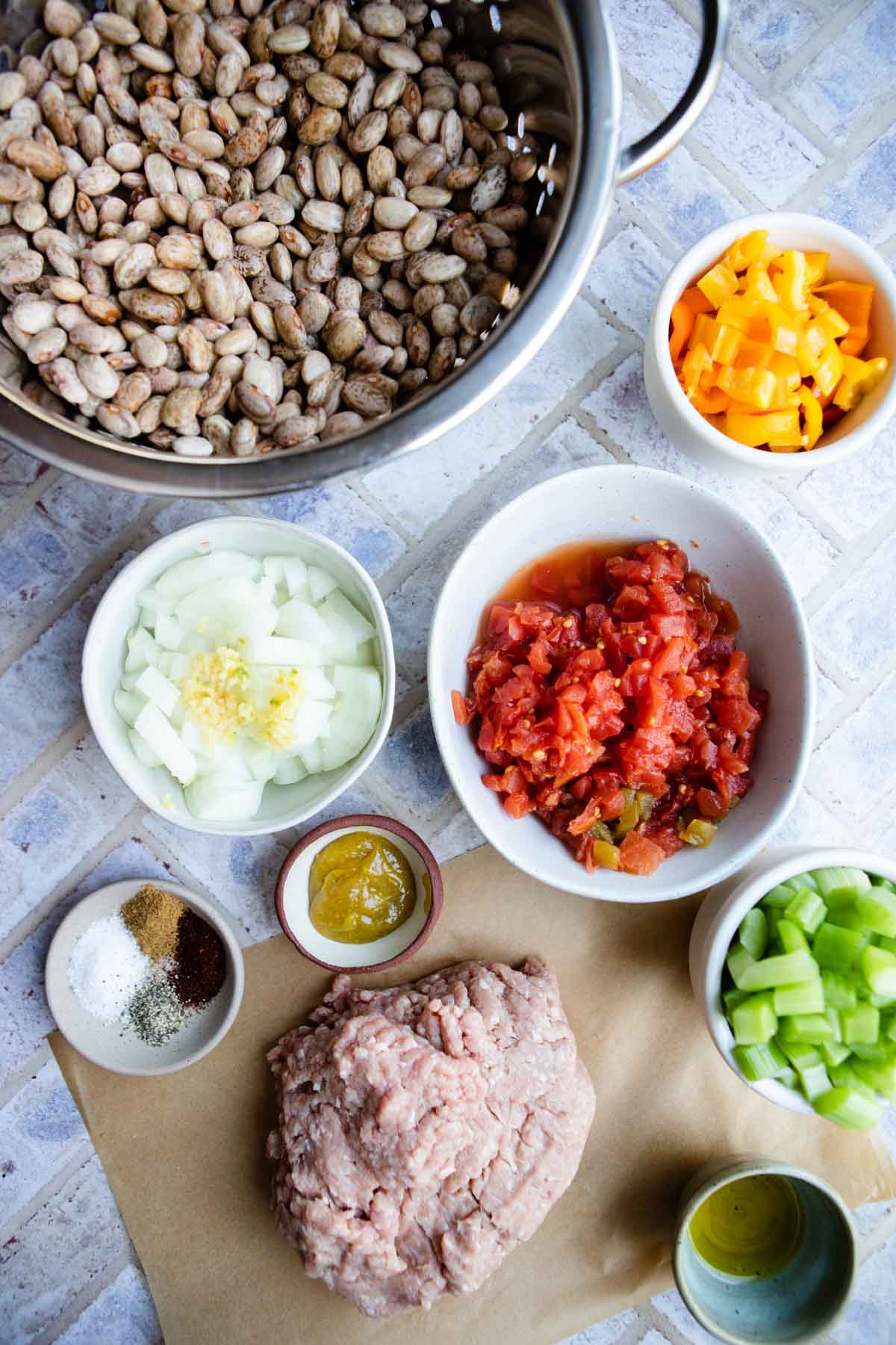 raw ground turkey, dried pinto beans, canned tomatoes, onions and celery and peppers in small bowls 