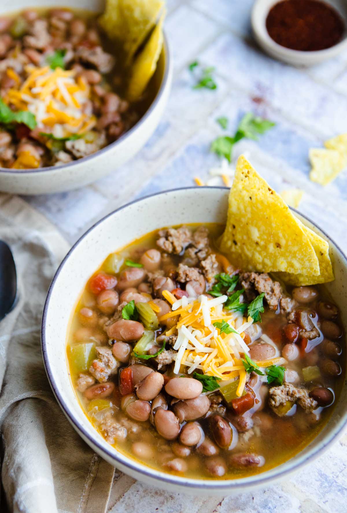 Instant Pot Bean soup in a beige bowl with shredded cheese and tortilla chips as a garnish