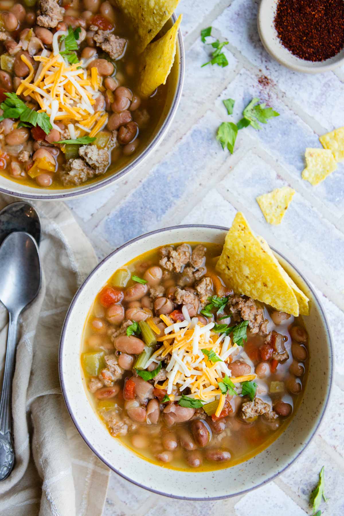 2 beige bowls filled with instant pot bean soup and garnished with cheese and chips 