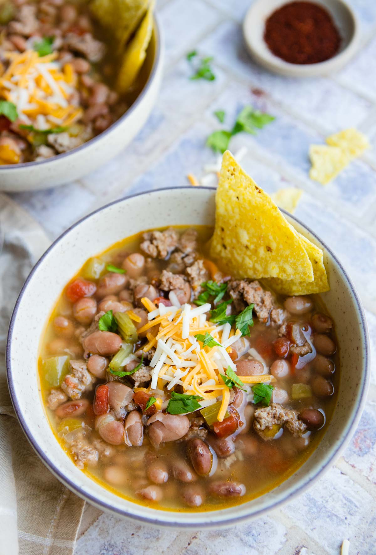 cooked beans and ground turkey served in a bowl garnished with cheese and tortilla chips 