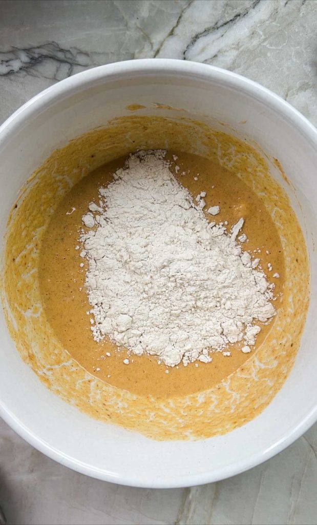 flour being added to pumpkin batter