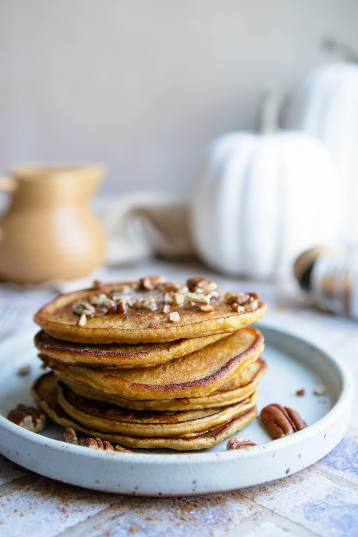 a stack of protein pumpkin pancakes drizzled with syrup and sprinkled with pecan pieces 