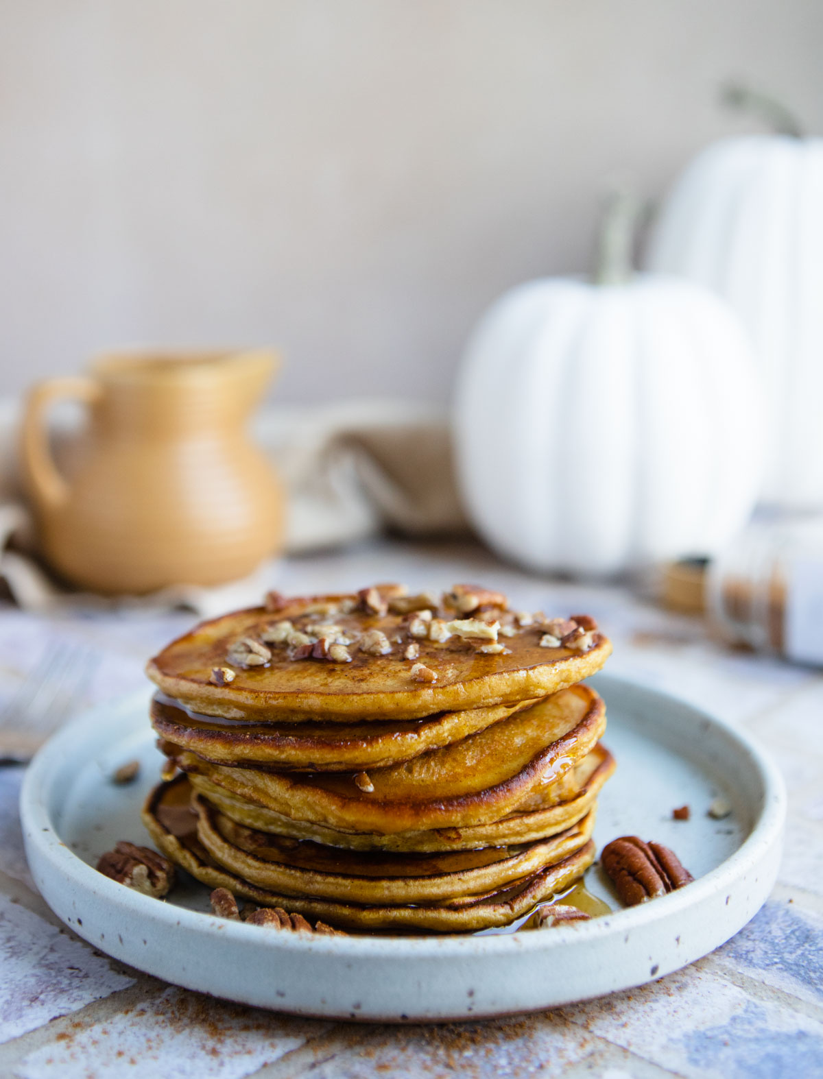 warm protein pumpkin pancakes stacked high on a gray plate and topped with nuts and syrup
