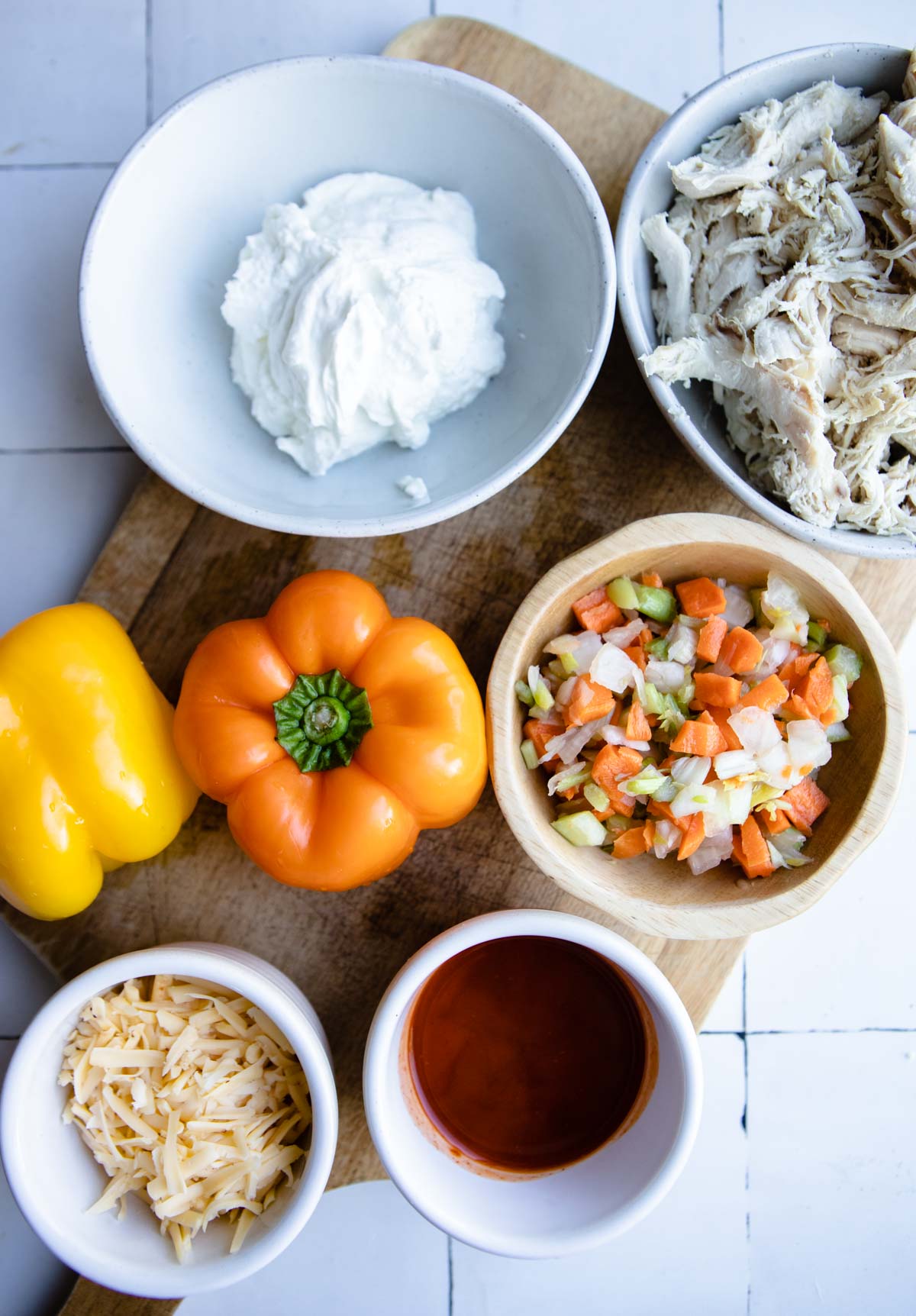 raw bell peppers, greek yogurt, shredded chicken. mixed veggies and buffalo sauce in small white bowls