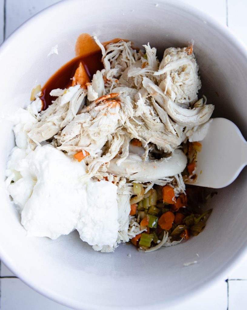 shredded chicken, veggies, greek yogurt and buffalo sauce in a white mixing bowl