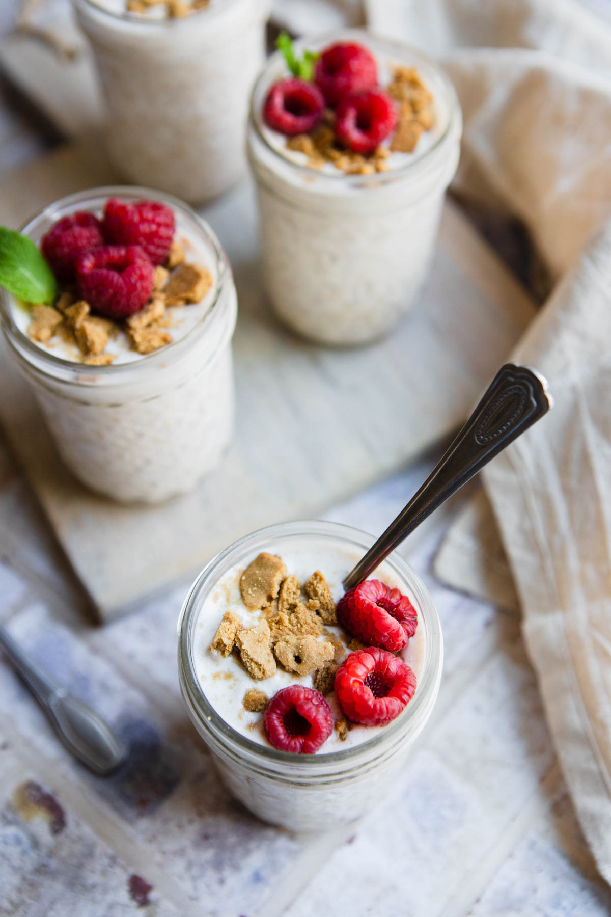 glass jars filled with overnight oats and topped with raspberries and graham cracker crumbles 