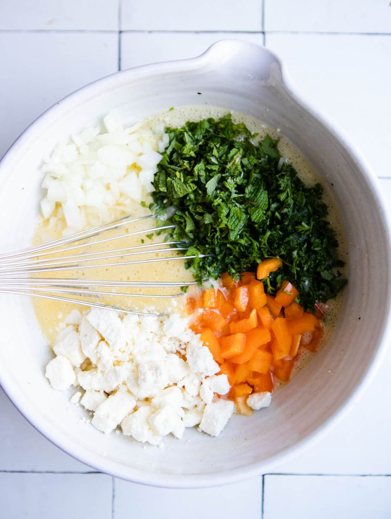 fresh herbs and veggies added to a large bowl with a cottage cheese egg mixture