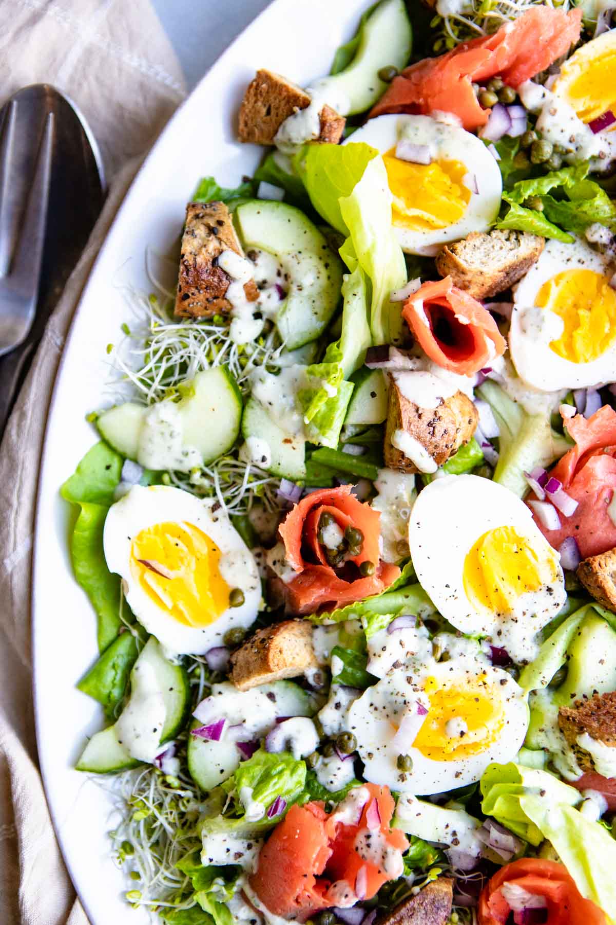 smoked salmon bagel salad with veggies, eggs and bagel on a platter and drizzled with dressing