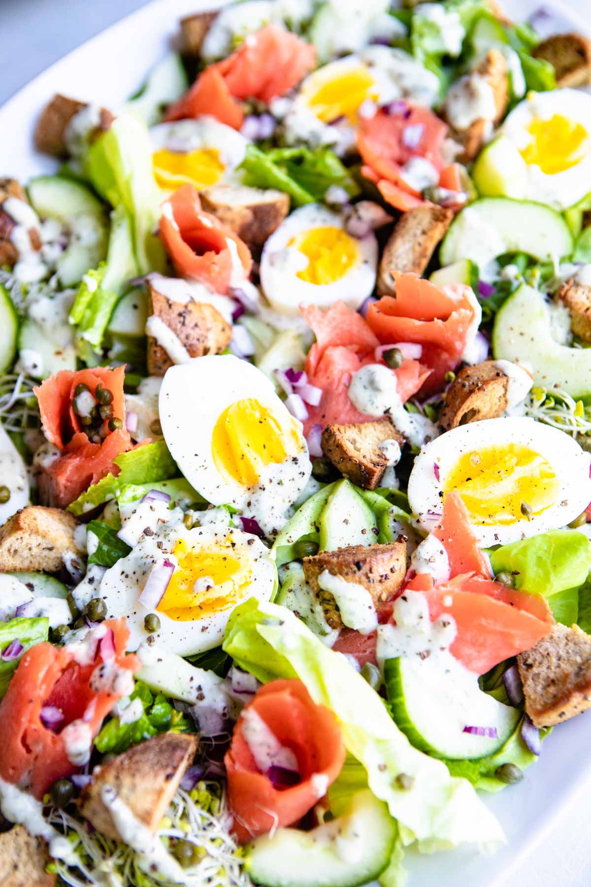 smoked salmon breakfast salad with hardboiled eggs, veggies and dill dressing on a white platter