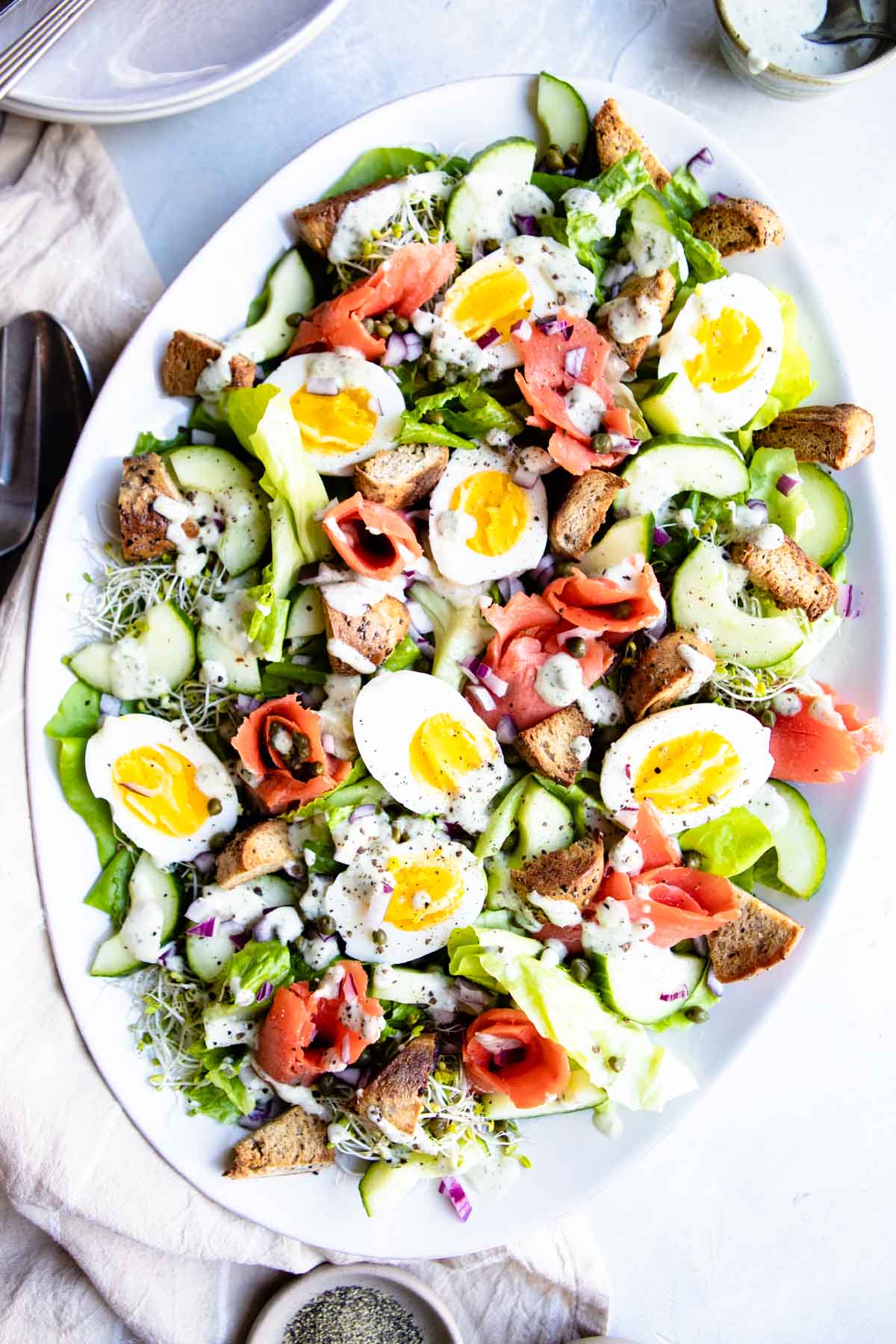 salad with dressing on a platter next to salad fork and tongs