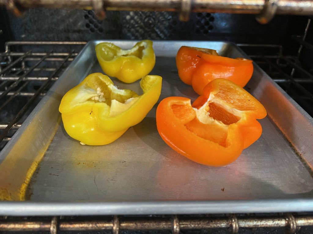 red and orange bell peppers on a sheet pan placed in the oven