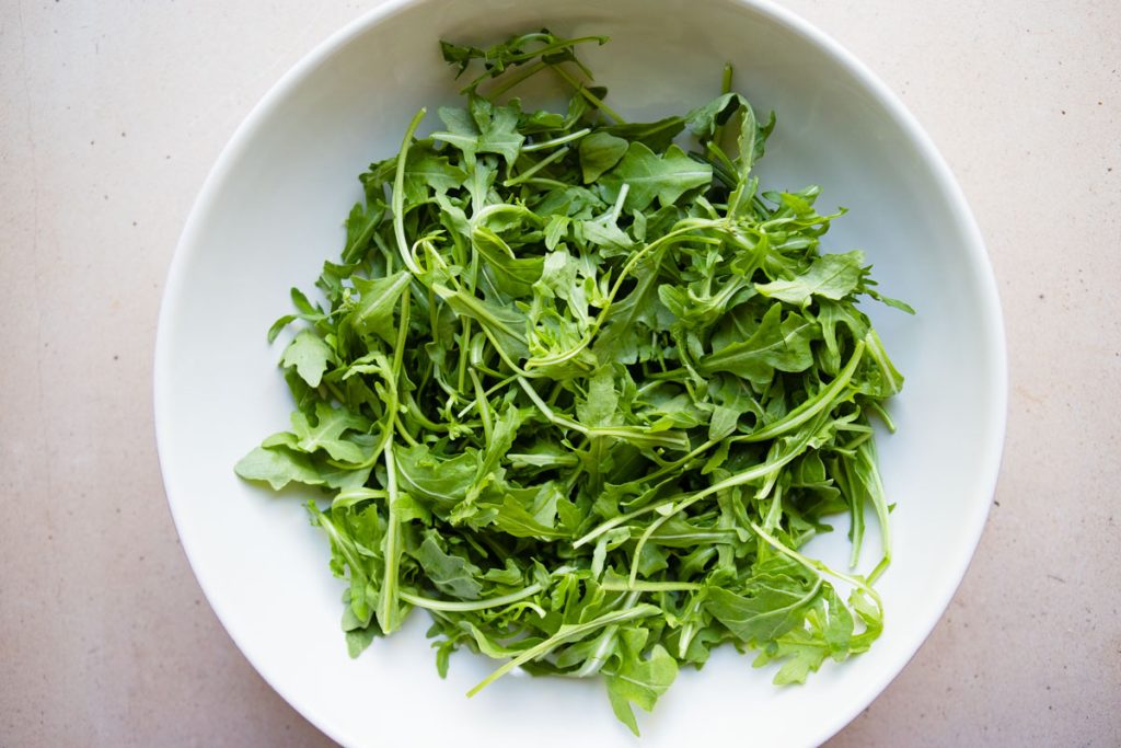 a large white bowl filled with arugula