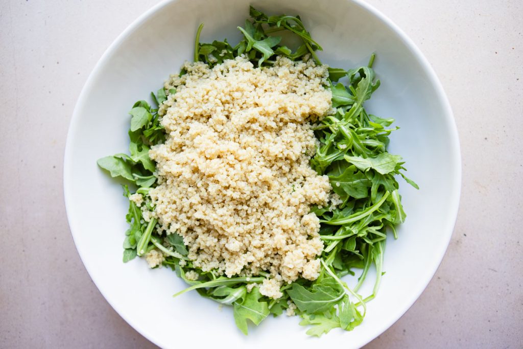 arugula leaves and cooked quinoa in a large white bowl