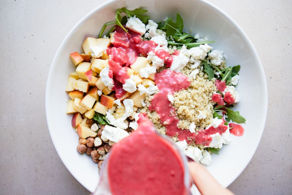 raspberry vinaigrette being poured on a arugula salad