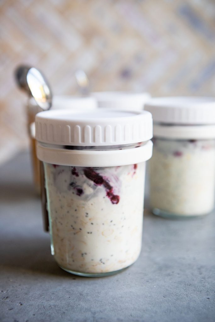 cute meal prep jars covered with a white lid and attached spoon, filled with overnight oats with frozen fruit