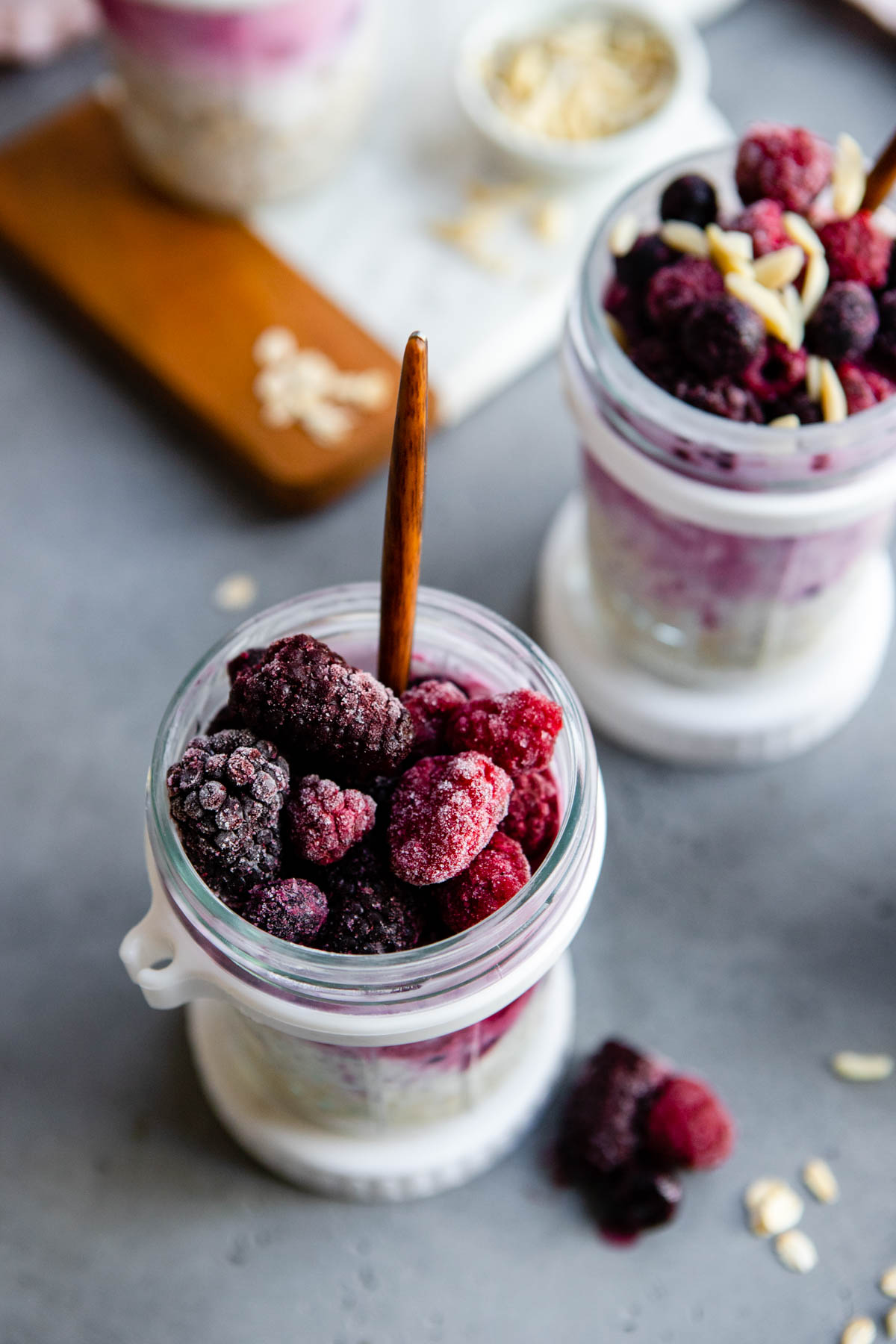 a jar of overnight oats topped with frozen berries and a wood handled spoon set inside the jar