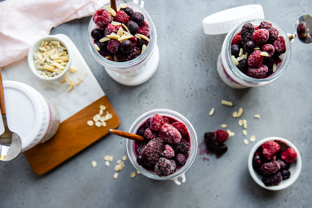 4 jars filled with overnight oats with frozen fruit and topped with nuts 