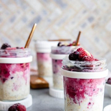 overnight oats with frozen fruit in meal prep jars on a gray surface